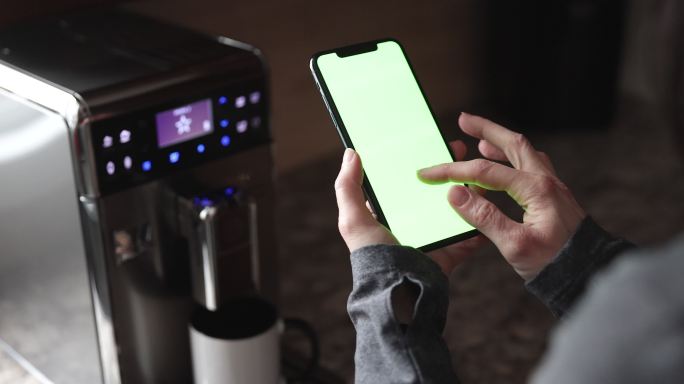 女性手持色度键绿色屏幕智能手机和煮咖啡的特写镜头