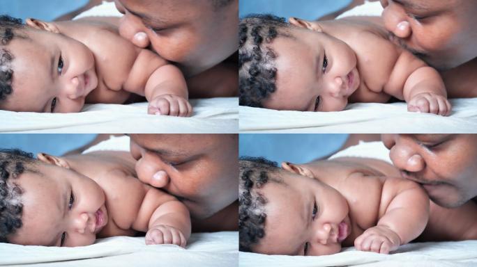快乐的非洲父亲在卧室亲吻3个月大的新生儿，而父亲和婴儿在一起的时刻。父亲节的概念。