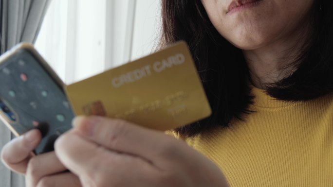 亚洲成年女性在家通过信用卡结账或在线购物，这是一种生活方式理念。