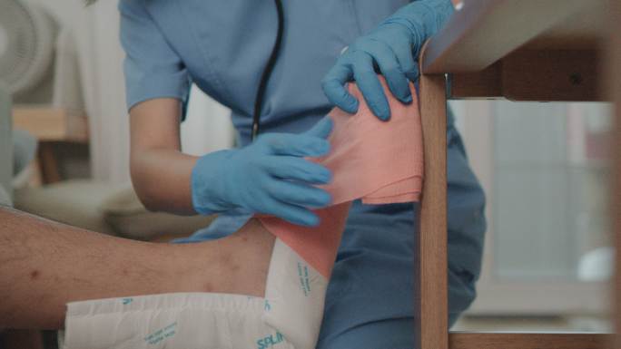 女护士给病人的腿缠上绷带。