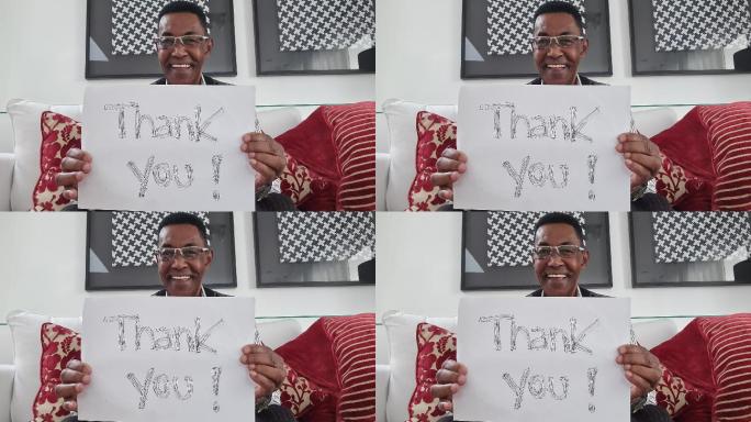 资深男士在视频通话中展示写有“谢谢”的论文-网络摄像头视角