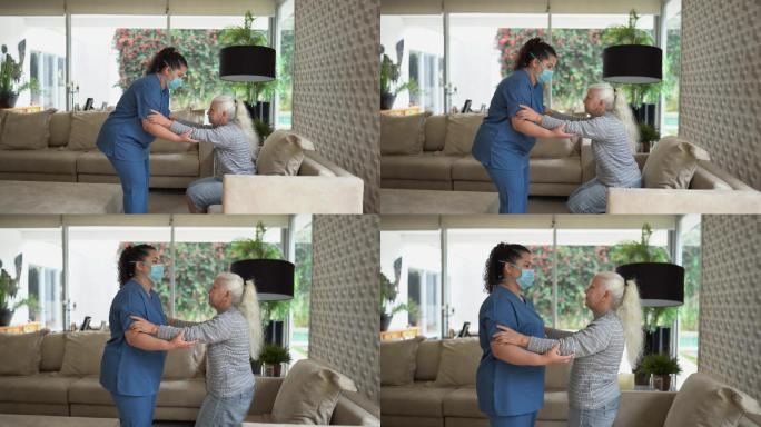 家庭护理人员帮助一位老年女性在家站立——医生戴着防护口罩