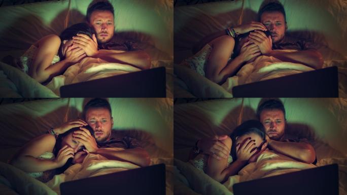 一对年轻夫妇在床上看恐怖电影。使用笔记本电脑，玩得开心