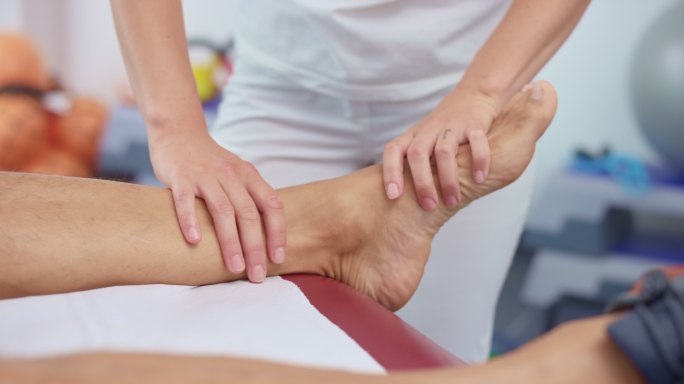 一位女性运动治疗师用SLO-MO的手按摩有问题的脚踝