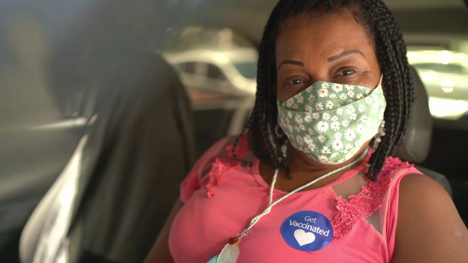 一位戴着“接种疫苗”贴纸、戴着口罩的快乐女性的肖像