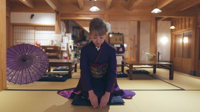 穿着“Furisode”和服的年轻女性坐在高跟鞋上，在日本的“榻榻米”房间鞠躬