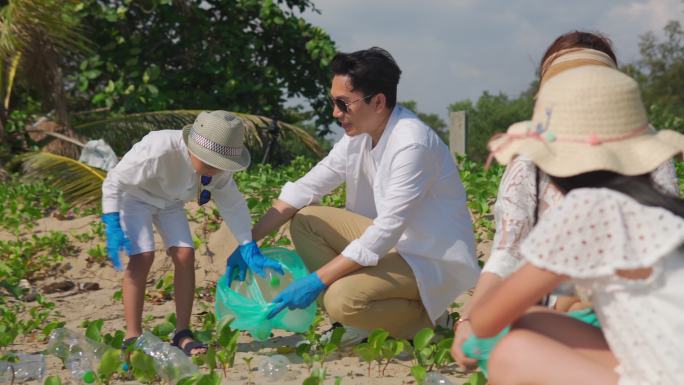 快乐的亚裔家庭和垃圾袋一起清理海滩上的区域。