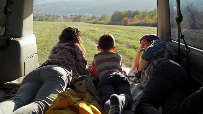 一对年轻夫妇和他们的儿子正在露营车的后部休息，欣赏风景