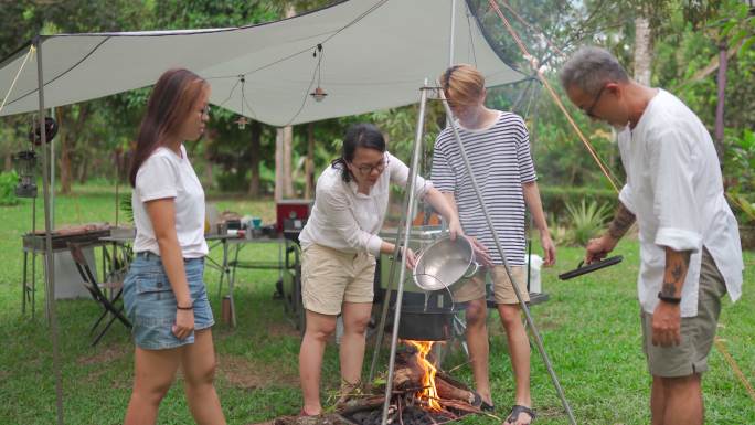 亚裔中国母亲在家人的帮助下，把水倒进锅里煮汤，点燃篝火，准备做饭
