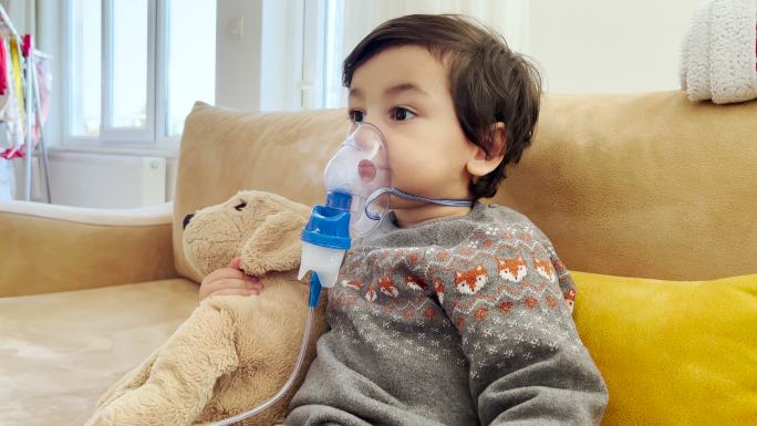 生病的蹒跚学步的男孩在家里用喷雾器和吸入器进行吸入