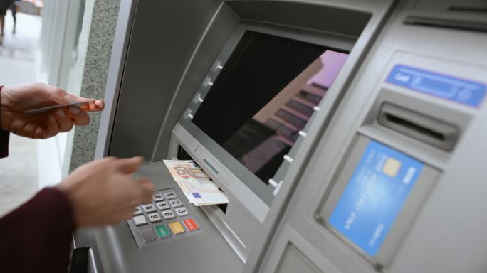 一位老妇人从ATM机取款口取出她的卡，数着她取款的钱