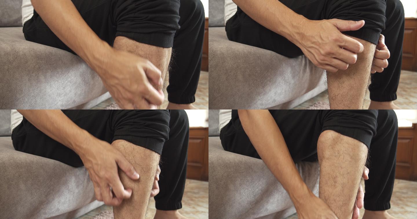 4k分辨率的亚裔男子坐在家里的沙发上，用手挠痒痒的腿。虫咬痛。医疗保健概念。