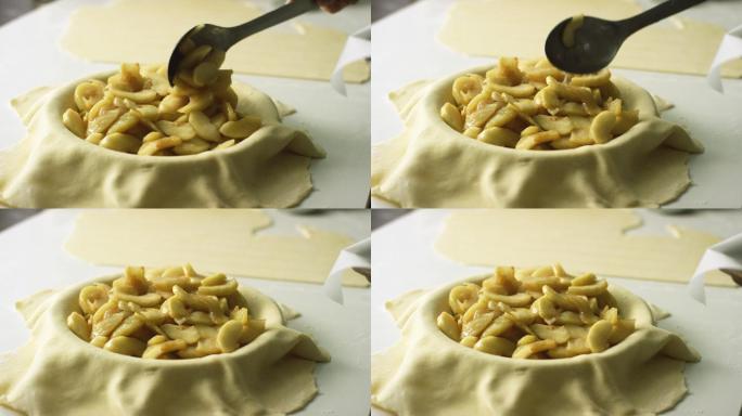 一个人在做苹果派的时候，用一个大金属勺子把煮熟的和去皮的苹果片（馅料）从盖着烤盘的烤盘里舀到盖着糕点
