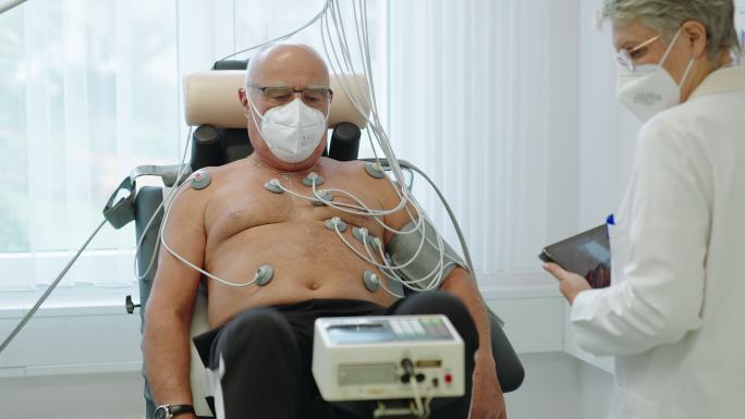 心脏病专家医生在诊所里用心电图自行车与一位老年患者交谈