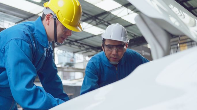 两名亚裔汽车修理工戴着头盔在修理厂工作。车辆服务经理团队男性工人打开汽车引擎盖，然后在车间检查和维修