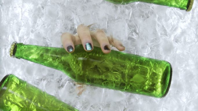 一个女人的手从一个冰容器里拿出一个绿色的啤酒瓶