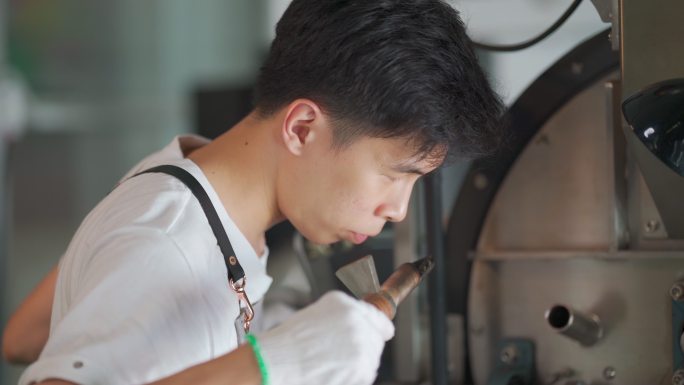 亚裔中国工匠微笑着拿着提尔从咖啡烤箱中提取咖啡豆烘焙生咖啡豆闻起来检查烘焙过程
