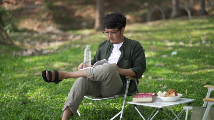 年轻人在野餐桌旁看书喝水。