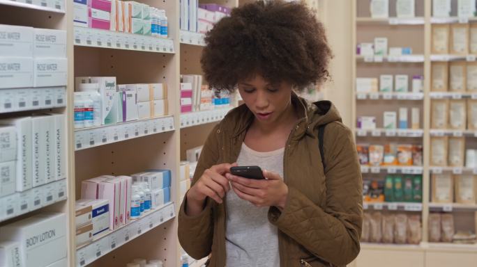 这名年轻女子在从药店货架上拿药瓶之前检查了手机