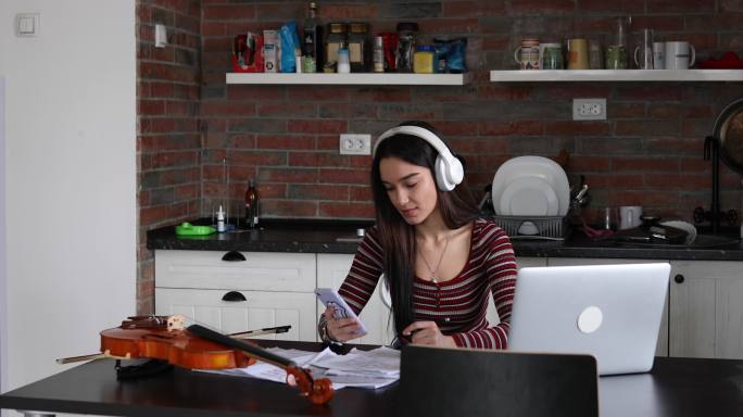 这位年轻的小提琴手用手机和耳机听一首曲子，稍后她将学习演奏。
