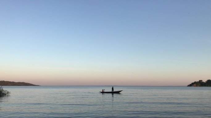 一个非洲渔夫和一艘旧木船划过湖面