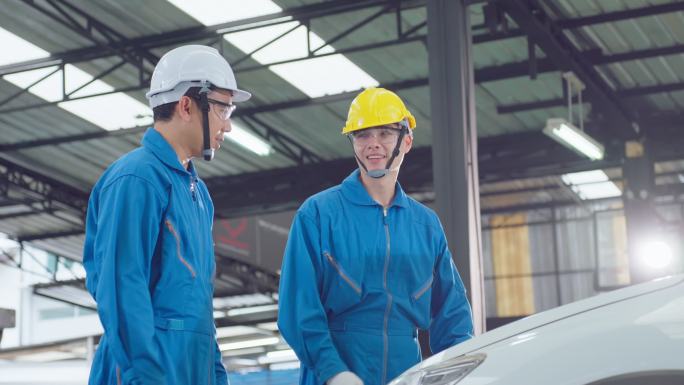 两名亚裔汽车修理工戴着头盔在修理厂工作。车辆服务经理团队男性工人打开汽车引擎盖，然后在车间检查和维修