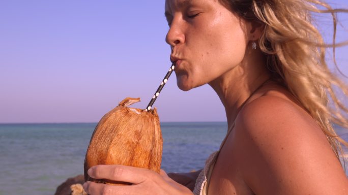 快乐的女人在海滩上享受椰子汁。