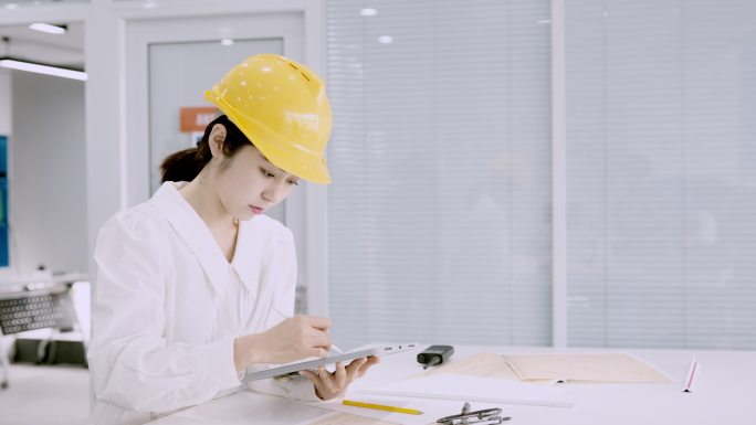 年轻漂亮的亚洲女工程师，戴着黄色头盔，使用平板电脑设计