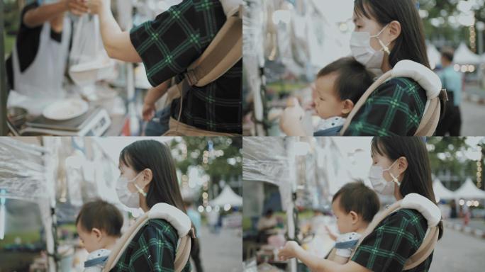 年轻的亚洲母亲抱着儿子购物，喜欢在街头小吃