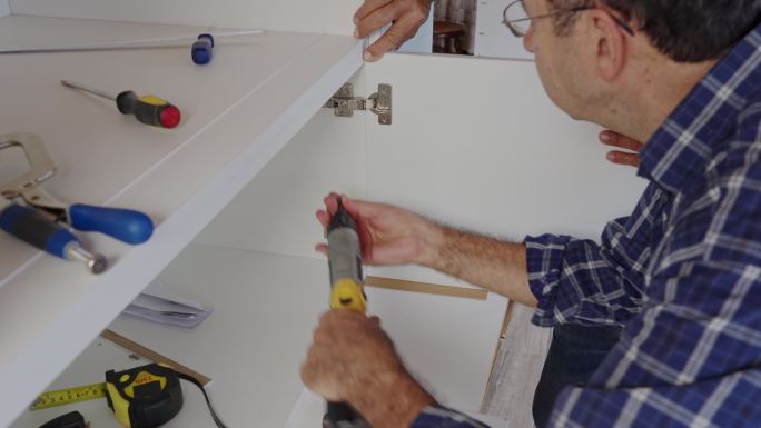西班牙裔高级木匠在自己的房子里为厨房装修安装橱柜铰链。