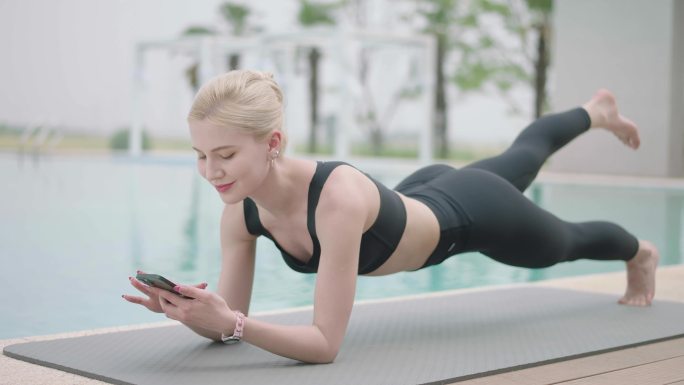 美女在泳池旁边练瑜伽边玩手机