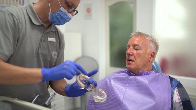 牙医拿着假牙，在牙医办公室与患者交谈