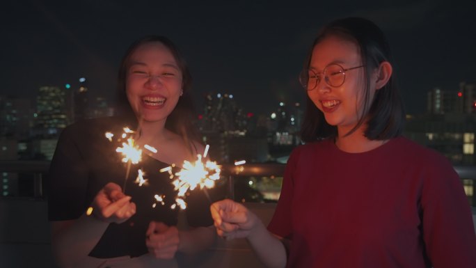 年轻的亚洲女性在酒吧与密友点燃火花庆祝，在千禧一代辛勤工作后，在屋顶派对上一起欢笑，感受快乐，放松身