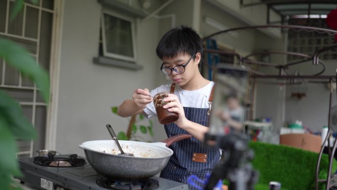 在后院厨房教烹饪广播的中国亚裔少年。