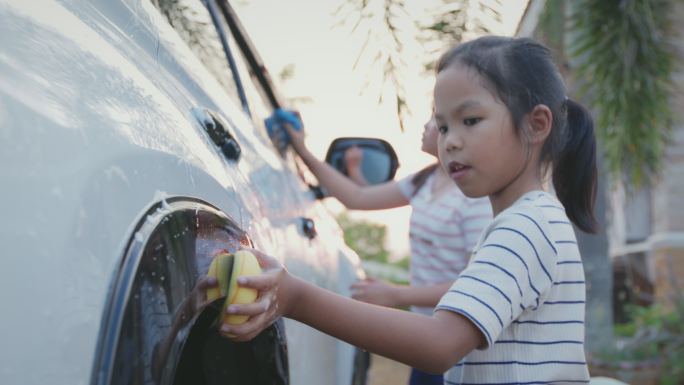 日落时分，亚洲小女孩和妹妹在家里用海绵和阳光一起帮父母洗车。