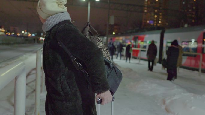 登机时间。在冬天寒冷的雪夜里，一位带着行李的成熟女性，一位游客，正在铁路站台上等待一列上车。她环顾四
