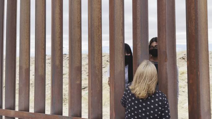 墨西哥妇女通过墨西哥和美国之间的国际边界屏障与戴着新冠病毒-19口罩的美国妇女交谈