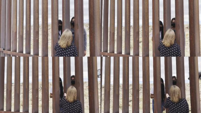 墨西哥妇女通过墨西哥和美国之间的国际边界屏障与戴着新冠病毒-19口罩的美国妇女交谈