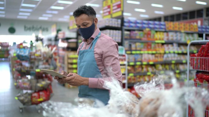 成年男子戴口罩用数码平板电脑控制超市库存