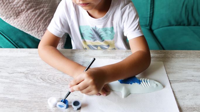 孩子用刷子和蓝色蛋彩画画石膏鲨鱼