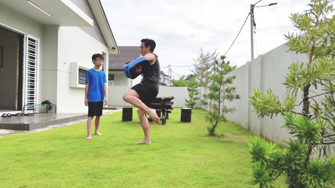 亚洲华人父亲运动员在花园训练儿子跆拳道。泰拳、武术