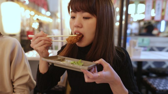 日本年轻女子在Izakaya酒吧吃炸鸡