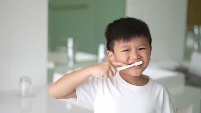 亚洲小孩在洁白干净的浴室刷牙。日常健康和牙科护理的概念