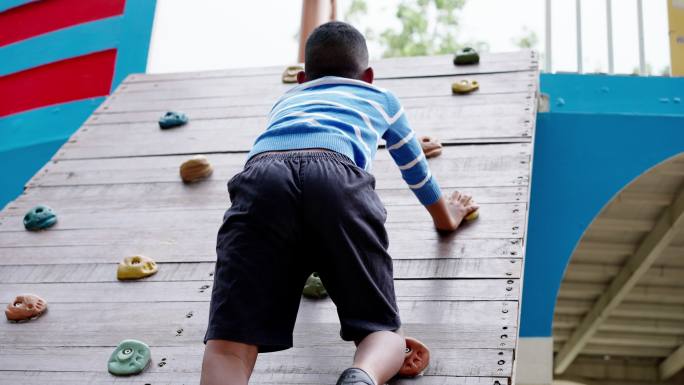非洲黑人儿童在公园、操场上玩耍的后视图。一个7岁的男孩在攀岩墙上。孩子玩得很开心。