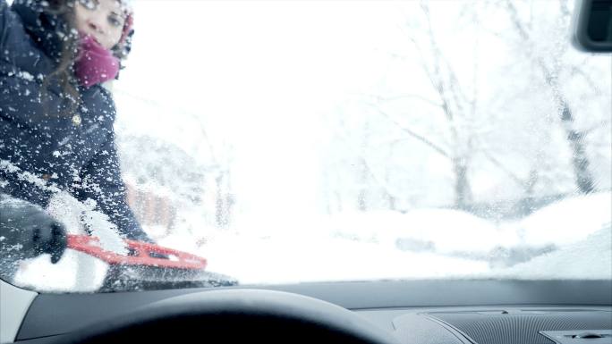 一个女人在刮汽车挡风玻璃上的雪。