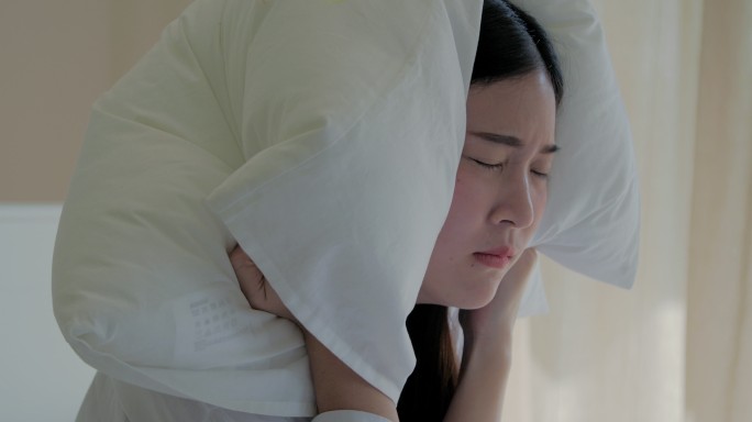 一大早，一位年轻女子试图在床上睡觉时用枕头捂住耳朵