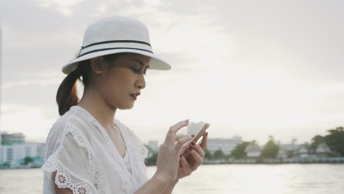 一名复古泰国女子在有遮阳的河边使用智能手机