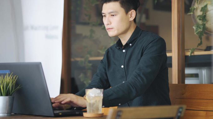 微笑的专业年轻亚裔华商在露天咖啡厅使用笔记本电脑