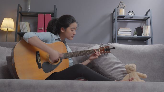 快乐的少女在家的客厅里弹原声吉他。创造性爱好