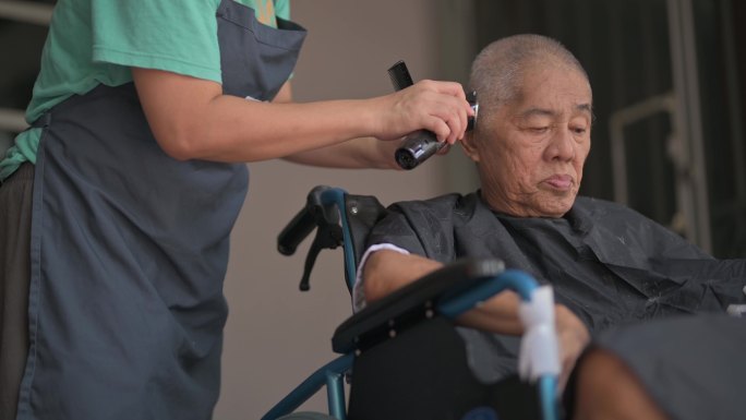 坐轮椅的亚裔中国老人在家前院理发